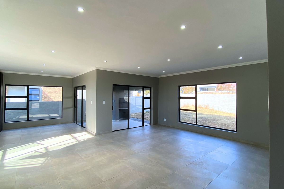Spacious, modern open-plan living area featuring neutral tiled floors, recessed downlighting, and large aluminium-framed windows providing ample natural light.