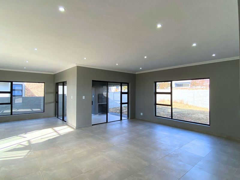 Spacious, modern open-plan living area featuring neutral tiled floors, recessed downlighting, and large aluminium-framed windows providing ample natural light.