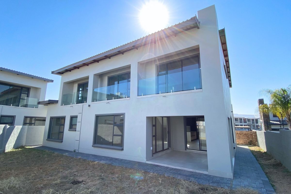Rear view of a modern double-storey house featuring glass balustrades, aluminium window frames, and a ground-floor patio area.