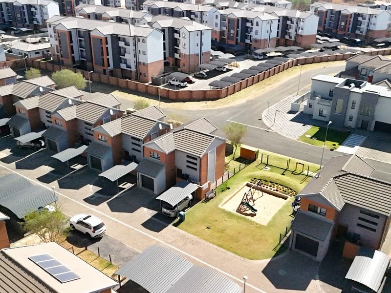 Aerial view of a modern townhouse complex featuring paved driveways, carports, communal playground area, and residential units with tiled roofs.