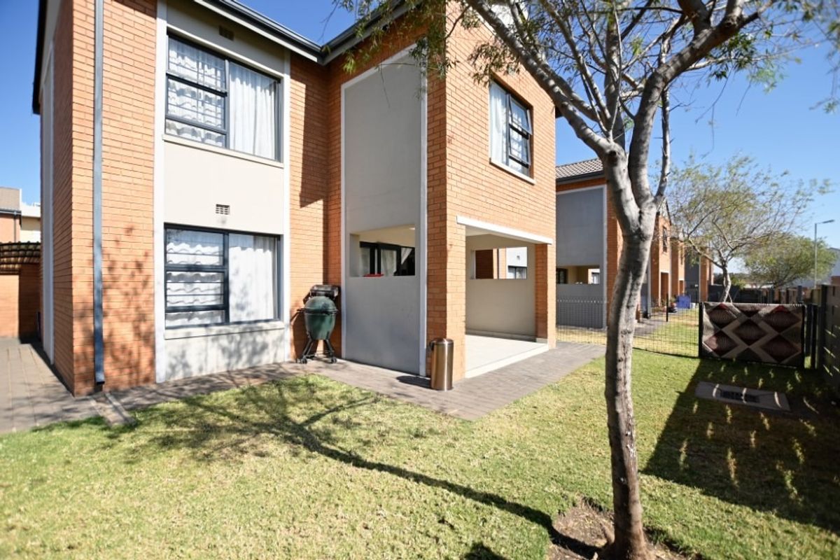 Rear view of the townhouse featuring a brick facade, a covered patio area, and a private garden with lawn and perimeter fencing.
