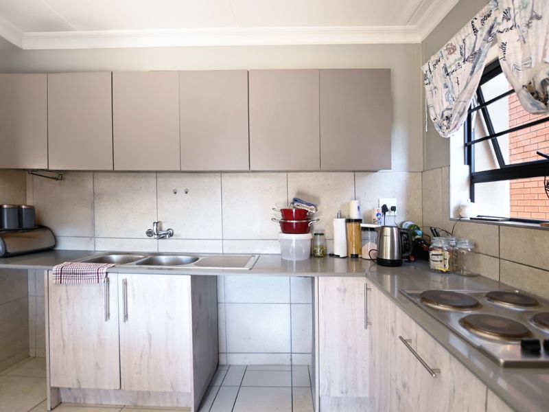 A functional kitchen featuring light wood-look cabinetry, a double sink, tiled splashbacks, and a built-in electric hob with ample counter space.
