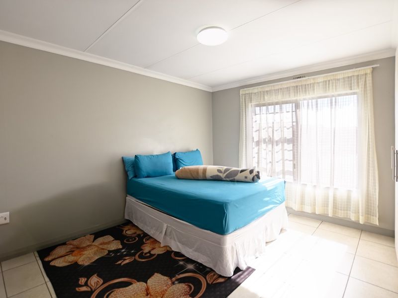 A functional bedroom featuring tiled flooring, a built-in wardrobe, and natural light through a large window.