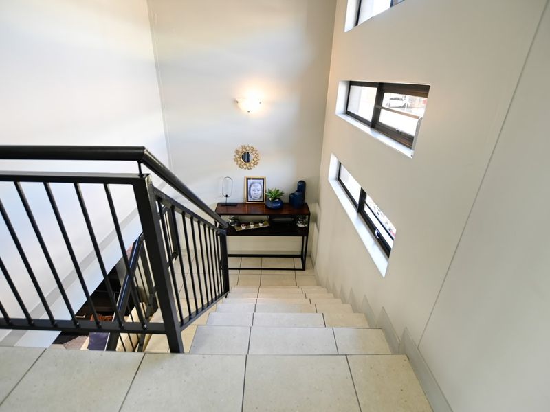 A bright, modern staircase featuring tiled steps, a black metal balustrade, and horizontal windows that allow for natural light.