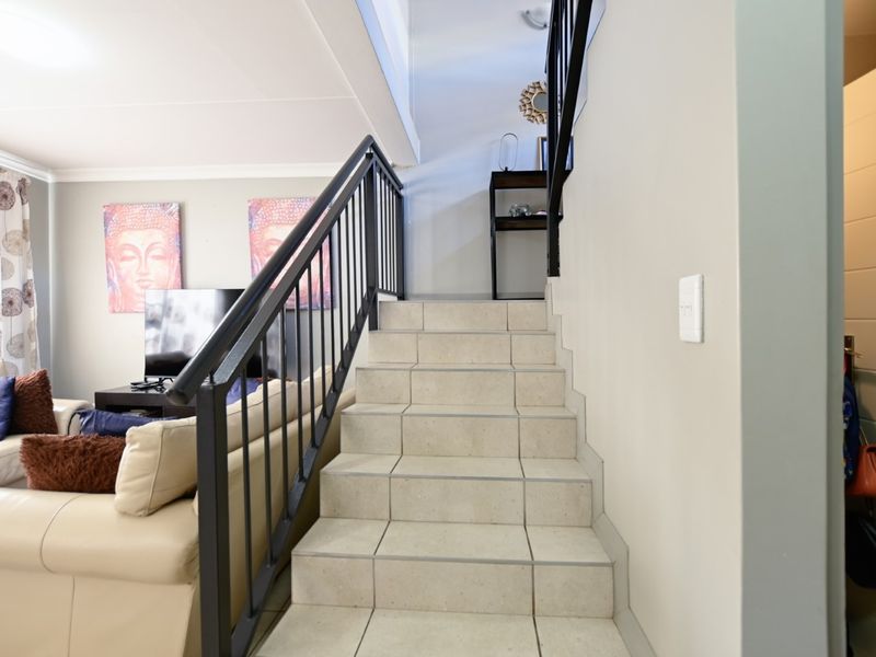 A view of the living area featuring a tiled staircase with a black metal balustrade leading to the upper level of the townhouse.