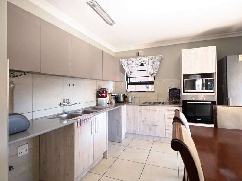 A functional kitchen featuring light wood-look cabinetry, a double sink, tiled backsplash, and built-in oven and microwave appliances.