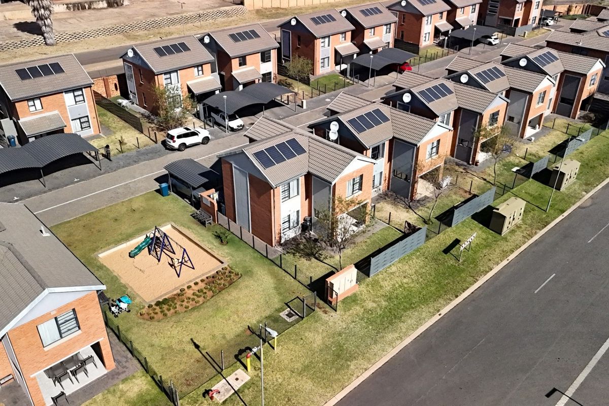Aerial view of a residential townhouse complex featuring brick buildings with tiled roofs, solar panels, private carports, and communal green spaces.