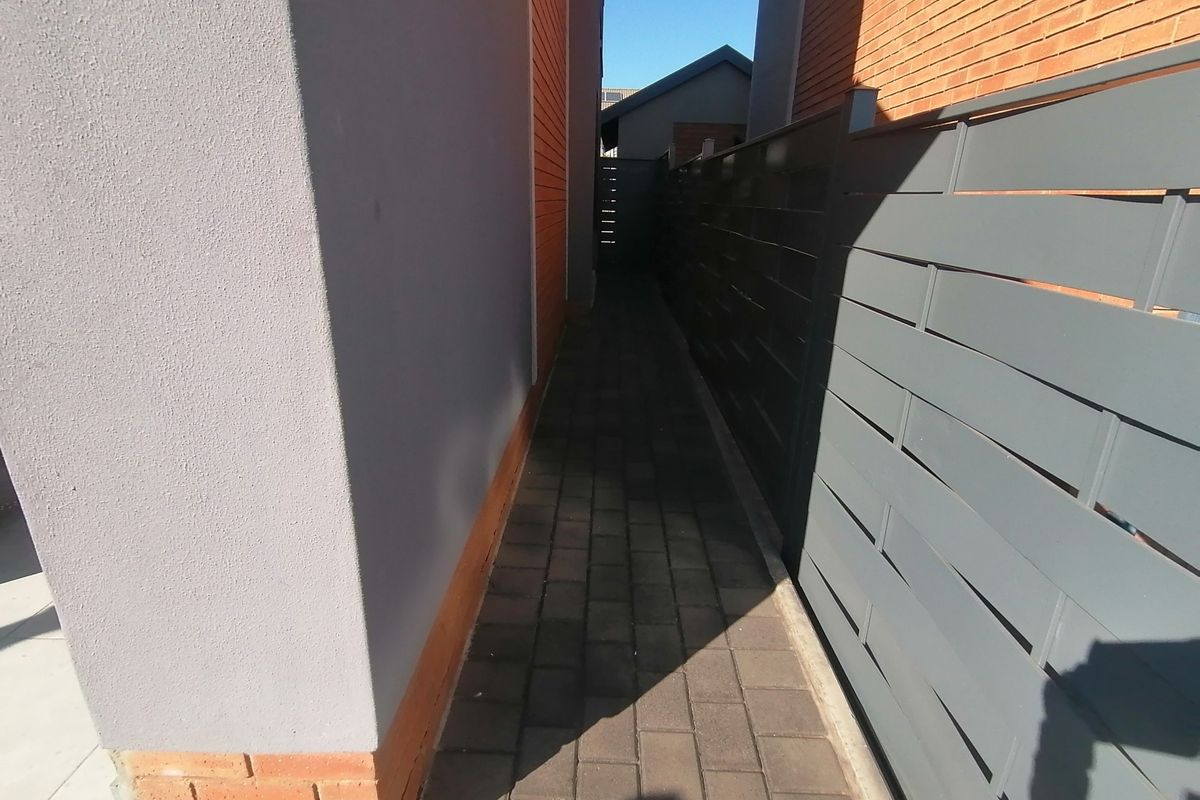 A narrow paved side passage between two townhouse structures, featuring modern horizontal slat fencing and a combination of brick and rendered wall finishes.