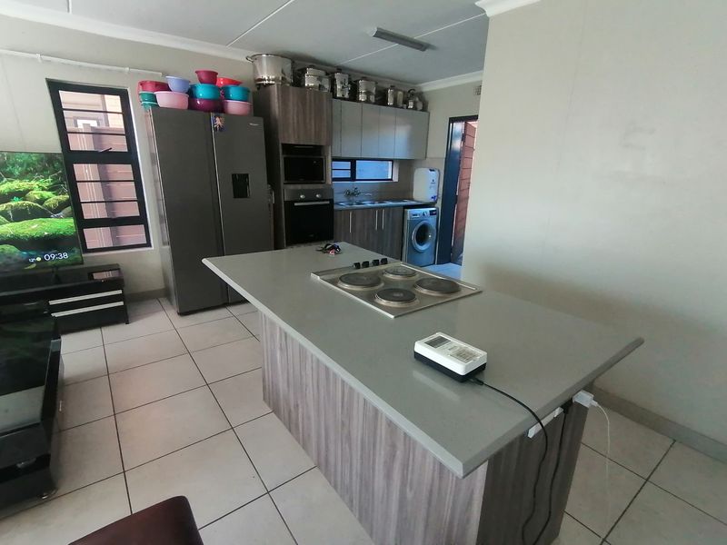 Open-plan kitchen featuring a central island with an electric hob, built-in oven, microwave, and tiled flooring, seamlessly integrated with the living area.