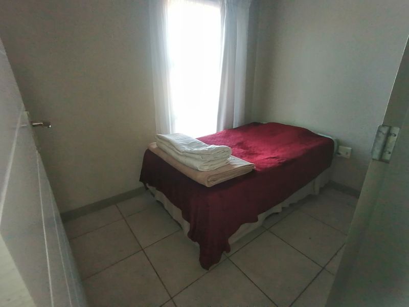 A compact bedroom featuring tiled flooring and a window, providing a functional space with neutral wall finishes.