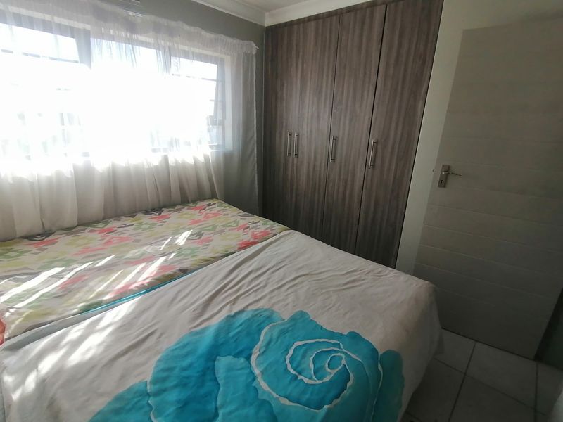 A bedroom featuring built-in wooden cupboards, tiled flooring, and natural light from the window.