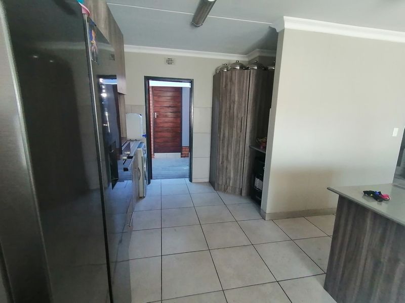 A functional kitchen area featuring built-in cabinetry, stone countertops, and tiled flooring, leading through to an adjacent room.