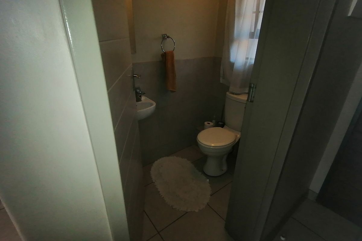 A compact guest bathroom featuring a toilet and a wall-mounted basin with neutral floor tiling.