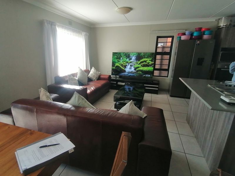 Open-plan living area featuring tiled flooring, a kitchen island with integrated appliances, and neutral wall finishes, creating a functional and connected living space.