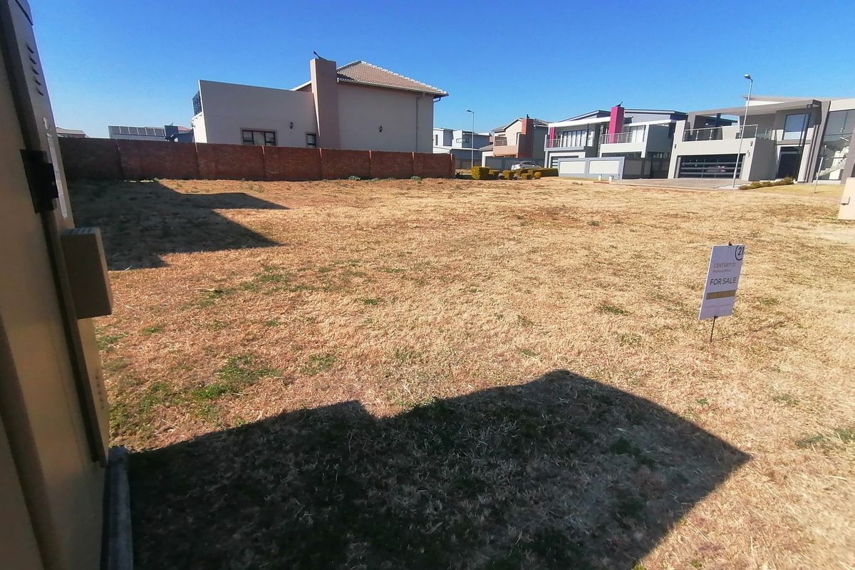 A vacant residential plot featuring a level grass surface and a brick boundary wall, situated within an established residential estate.