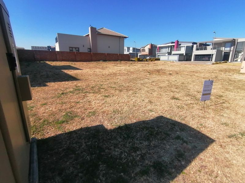 A vacant residential plot featuring a level grass surface and a brick boundary wall, situated within an established residential estate.