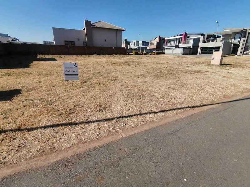 A vacant residential plot of land featuring a boundary wall and electrical connection point, situated in a developed neighborhood.