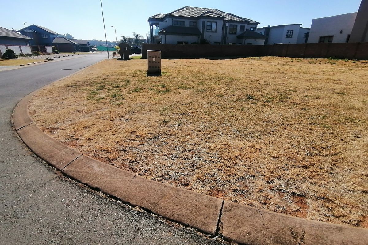 A vacant residential plot situated on a corner lot, featuring established kerbing, street lighting, and surrounding boundary walls in a developed neighborhood.