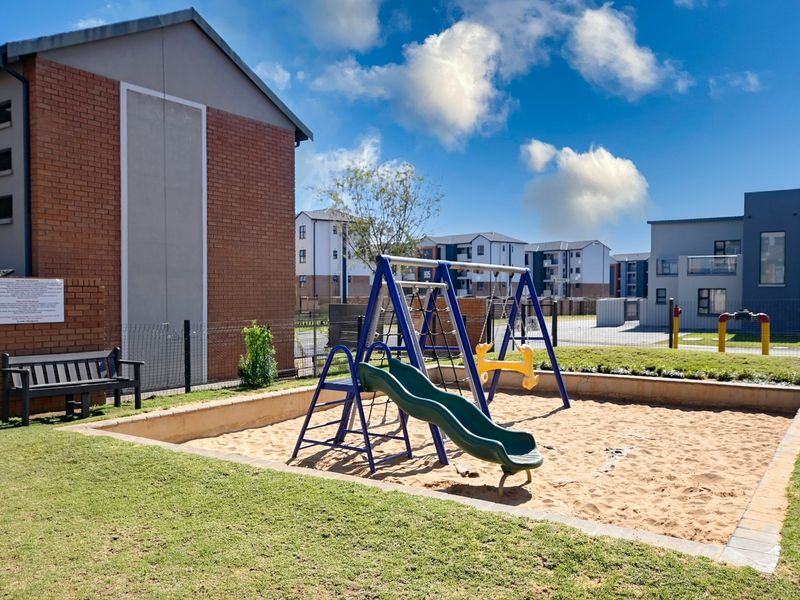 A well-maintained communal garden area featuring a sandpit and playground equipment, situated within a residential complex.