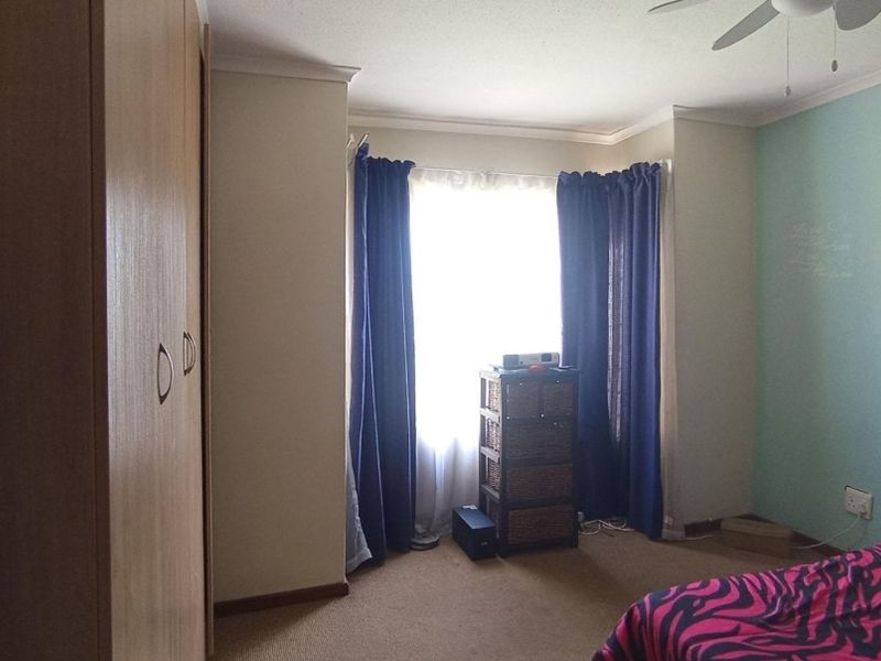 A bedroom featuring built-in cupboards, carpeted flooring, and a ceiling fan, with a window providing natural light.