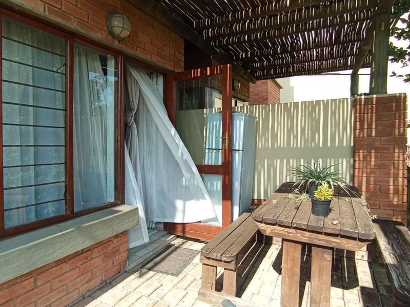 A covered outdoor patio area featuring brick walls, timber window and door frames, and paved flooring, providing a functional space for outdoor relaxation.