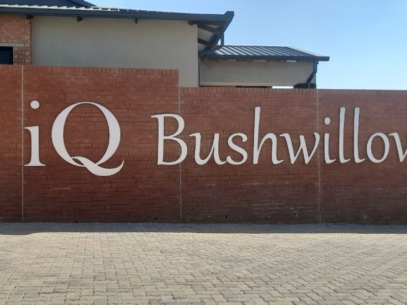 The entrance to the iQ Bushwillow townhouse complex featuring a prominent brick boundary wall and paved driveway.