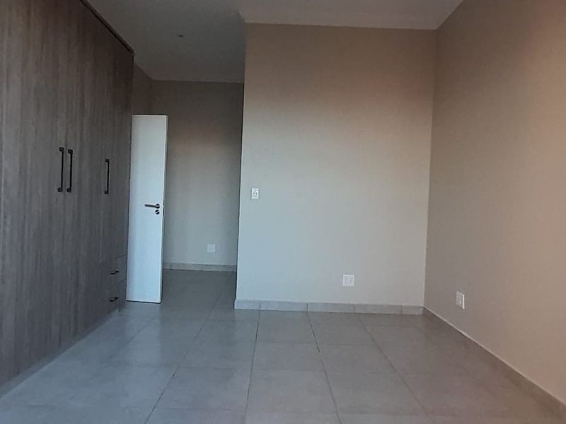 A spacious, empty bedroom featuring neutral tiled flooring and extensive built-in wooden cupboards, offering a clean and versatile living space.