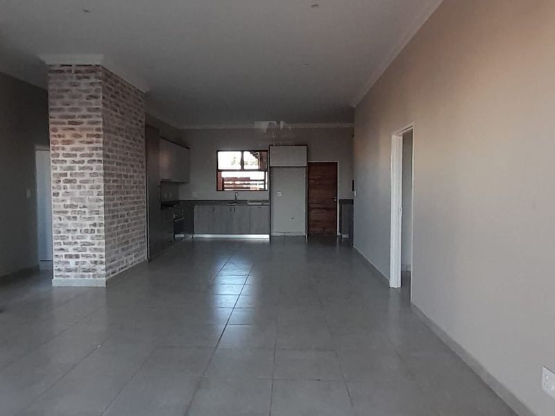 Spacious open-plan living and kitchen area featuring neutral tiled flooring, an exposed brick feature pillar, and modern built-in cabinetry.