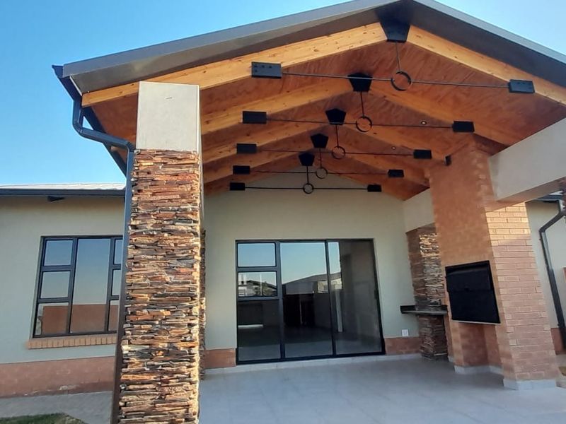 A spacious covered patio featuring stacked stone pillars, an exposed timber ceiling, and a built-in braai, providing an excellent outdoor entertainment area.