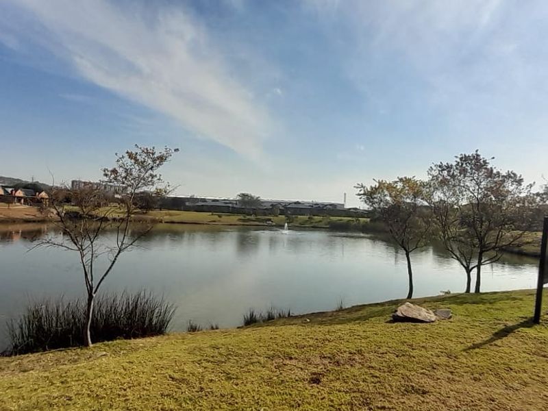 A scenic view of a tranquil estate lake surrounded by landscaped parkland and paved walking paths, offering a peaceful outdoor environment.