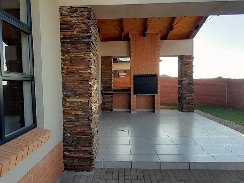 A spacious covered patio featuring stone-clad pillars, a built-in braai, and tiled flooring, offering an ideal space for outdoor entertaining.