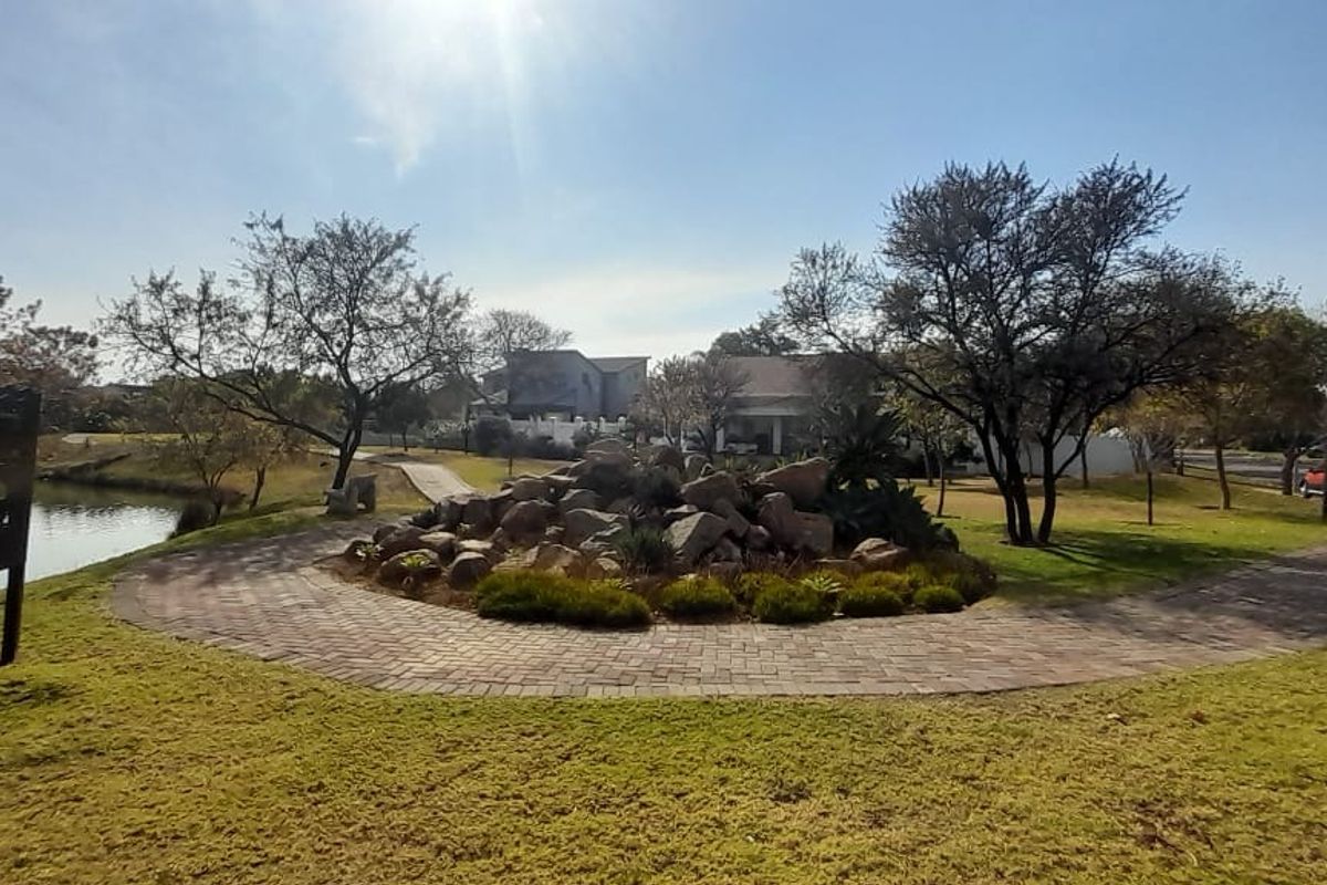 A well-maintained communal garden area featuring a paved walkway, landscaped rockery, and scenic lake frontage within the estate.
