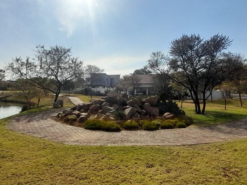 A well-maintained communal garden area featuring a paved walkway, landscaped rockery, and scenic lake frontage within the estate.
