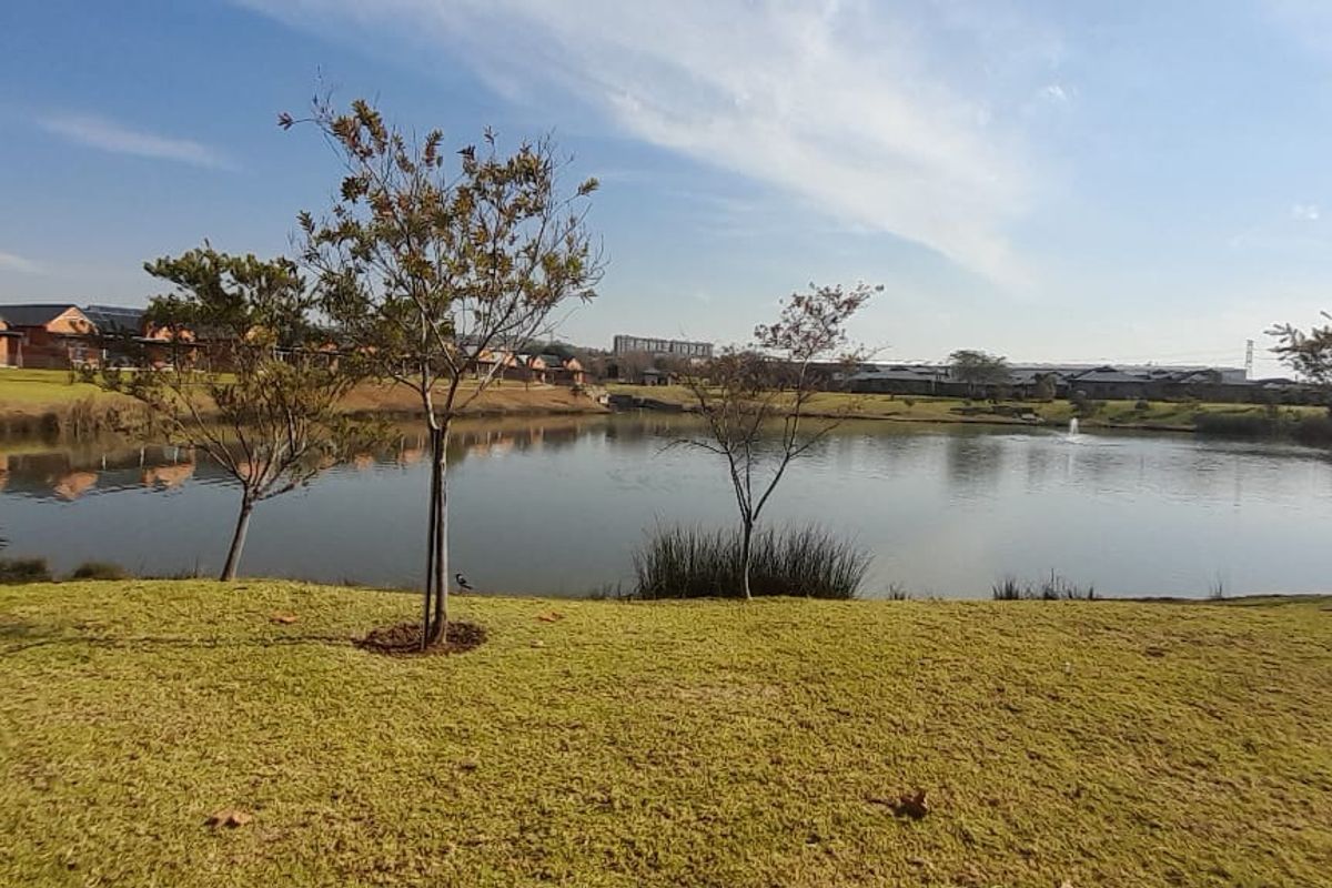 A scenic view of a tranquil estate lake surrounded by manicured lawns and mature trees, showcasing the peaceful outdoor environment of the townhouse complex.