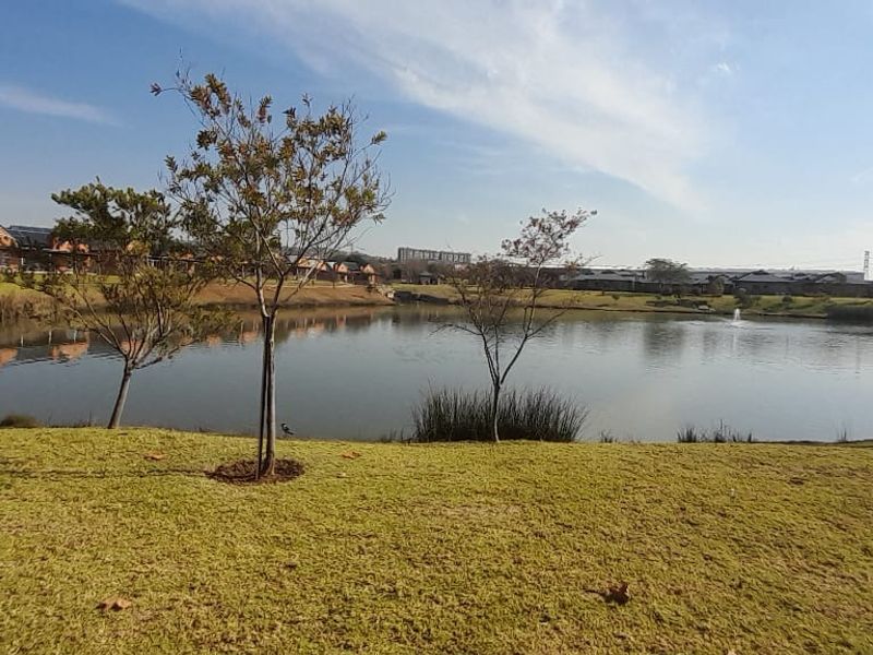 A scenic view of a tranquil estate lake surrounded by manicured lawns and mature trees, showcasing the peaceful outdoor environment of the townhouse complex.