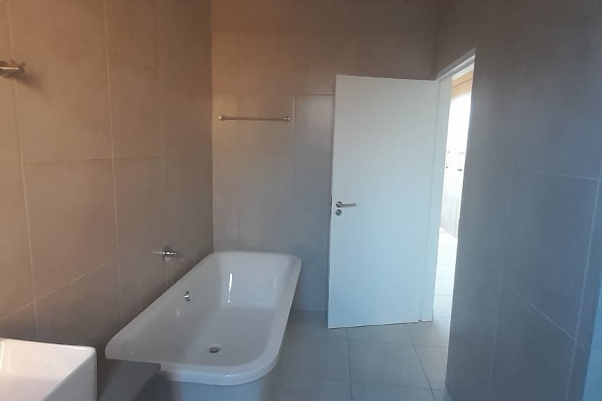 A modern, neutral-toned bathroom featuring a freestanding bathtub, wall-mounted basin, and full-height wall tiling.