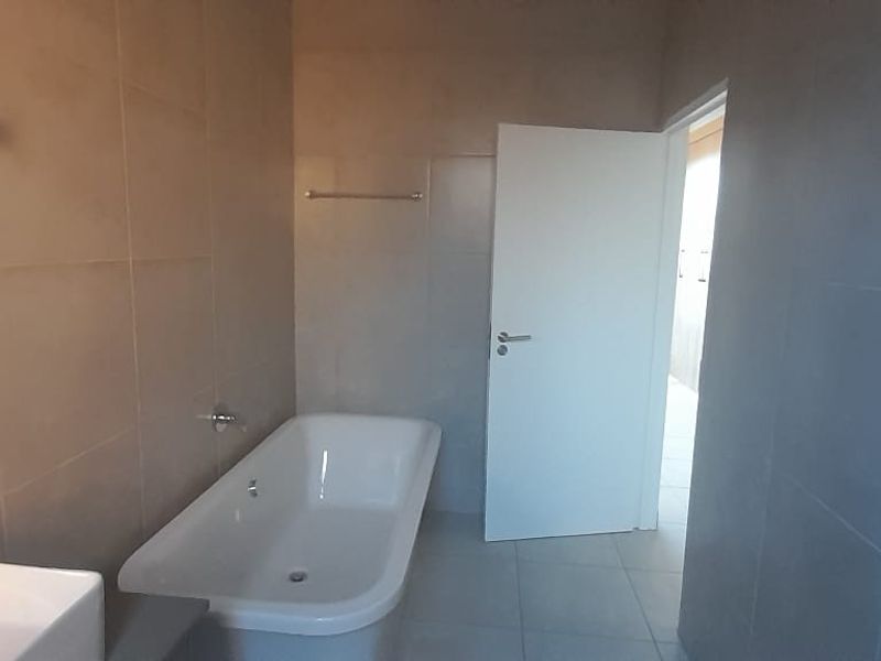 A modern, neutral-toned bathroom featuring a freestanding bathtub, wall-mounted basin, and full-height wall tiling.