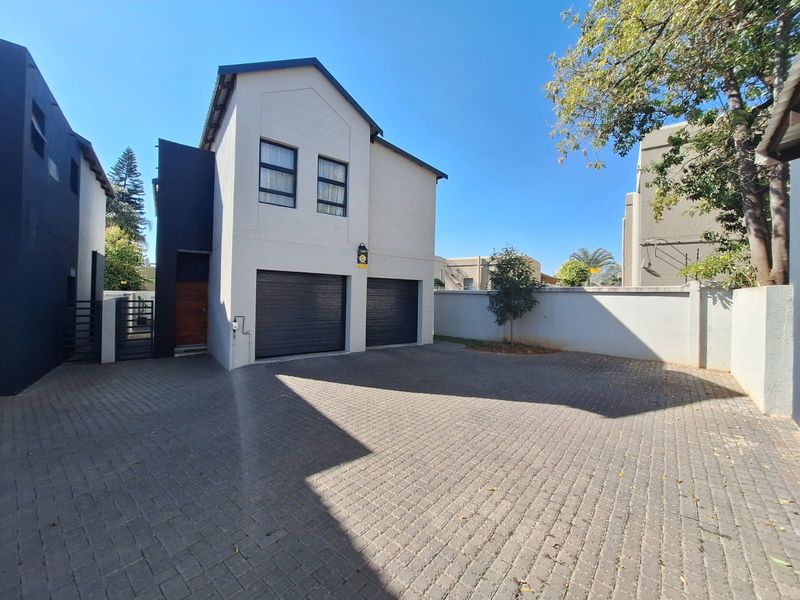 Front view of a modern double-story house featuring a double garage, paved driveway, and secure boundary walling.