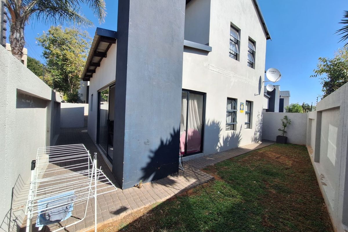 Rear view of a two-story house featuring a paved patio area, small garden, sliding glass doors, and secure perimeter walling.