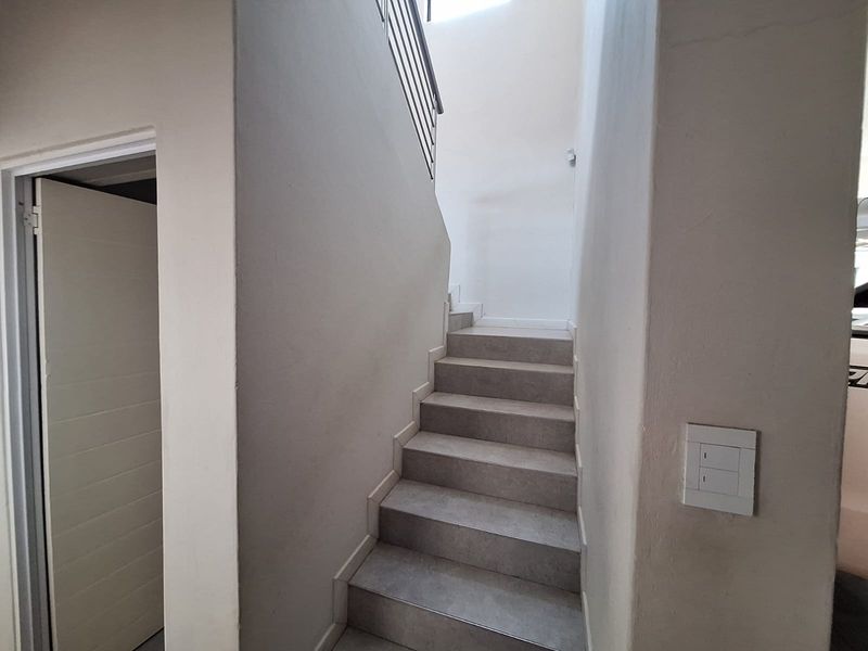 A clean, minimalist staircase featuring tiled steps and a modern metal balustrade, providing access between levels.