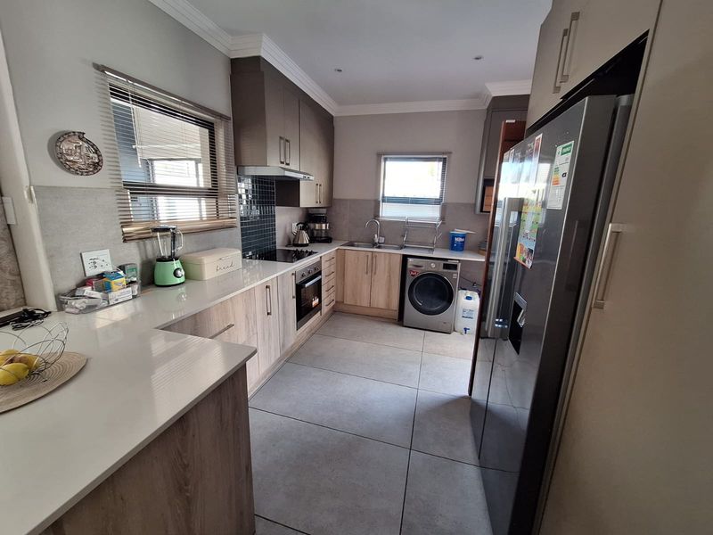 Modern kitchen featuring light wood-tone cabinetry, stone countertops, integrated appliances, and large format floor tiles with a clean, functional layout.