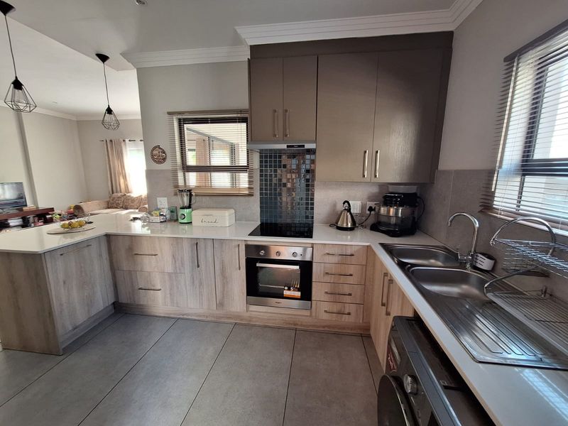 Modern kitchen featuring light wood-grain cabinetry, quartz countertops, a mosaic backsplash, and integrated appliances, seamlessly flowing into the adjacent living area.