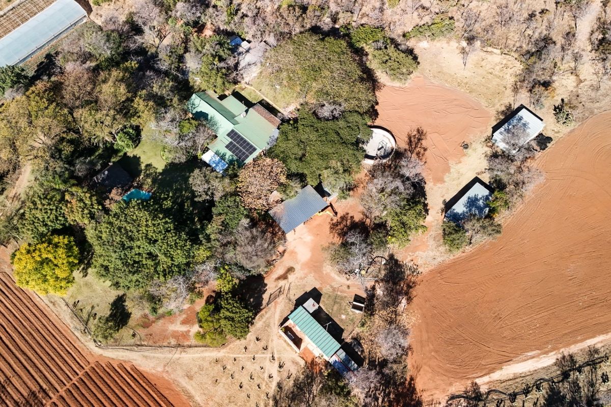 Aerial view of a small holding property featuring a main residence with solar panels, a swimming pool, multiple outbuildings, and surrounding agricultural land.