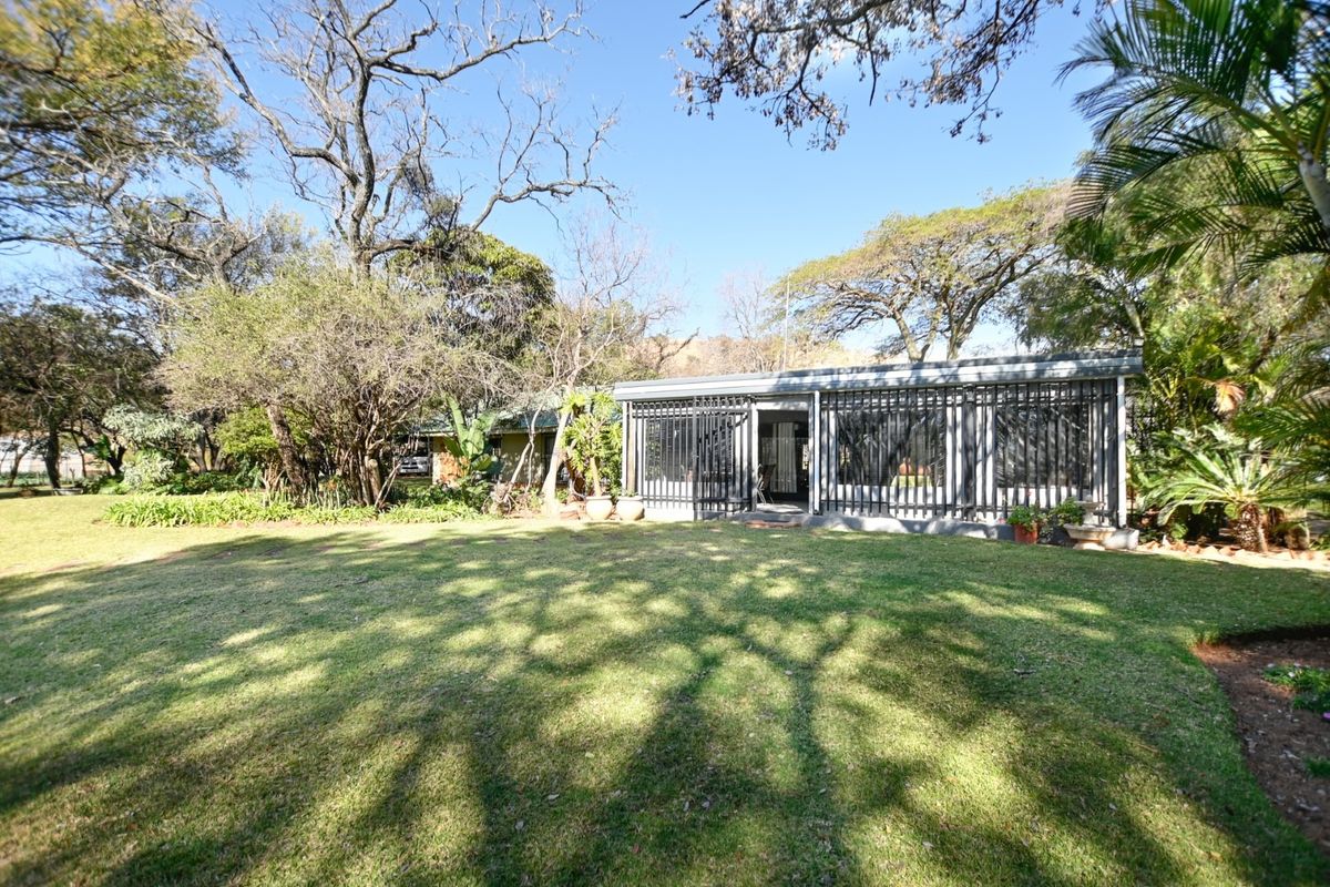 A view of the rear exterior of the property featuring a well-maintained lawn, mature trees, and a secure patio area with metal security gates.
