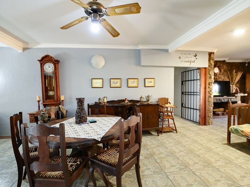 Spacious living area featuring tiled flooring, a ceiling fan, and a rustic stone fireplace, offering a warm and inviting atmosphere.
