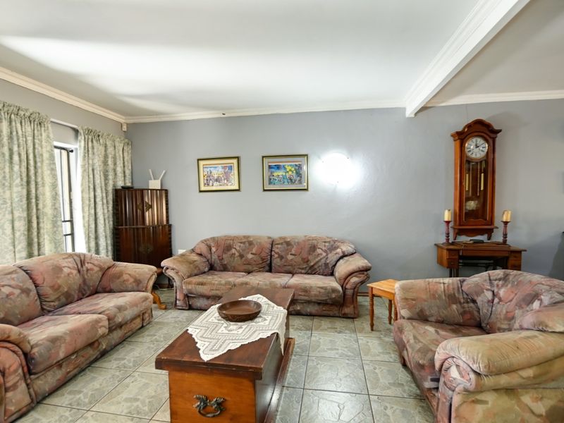 A spacious living room featuring neutral grey walls, tiled flooring, and classic ceiling cornicing, offering a comfortable and functional living space.
