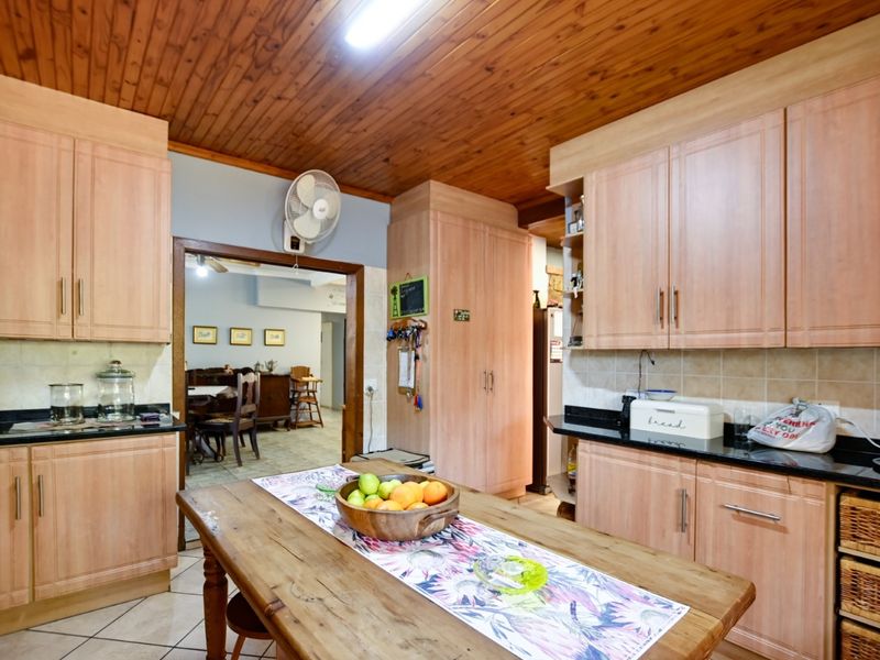 A functional kitchen featuring light wood-look cabinetry, dark granite countertops, tiled backsplash, and a distinctive timber-clad ceiling.