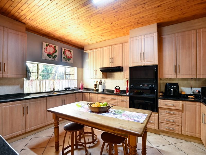 A functional kitchen featuring light wood cabinetry, dark laminate countertops, a built-in oven, and a distinctive timber-clad ceiling.