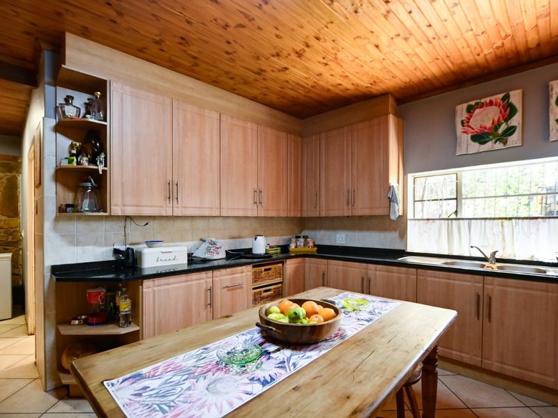 A functional kitchen featuring light wood cabinetry, dark stone countertops, a double basin sink, and a distinctive wooden tongue and groove ceiling.