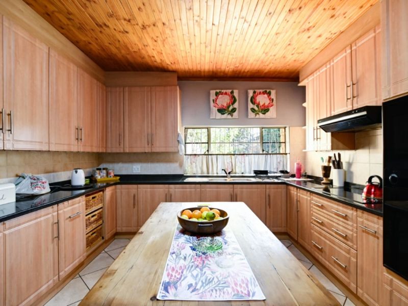 A functional kitchen featuring light wood cabinetry, dark granite countertops, a double sink, and a warm wooden tongue and groove ceiling.